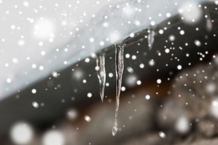 赛季摄影照片_季节，住房和冬季概念—冰柱和雪挂在建筑物屋顶。屋顶上悬挂的冰柱和雪