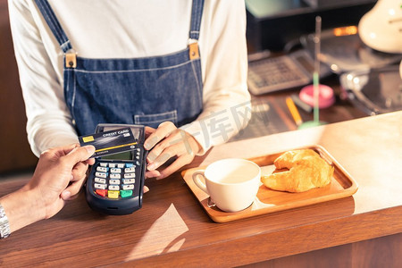 特写：一位亚洲顾客用他的信用卡和非接触式nfs技术在一家咖啡馆为他的咖啡师买咖啡付款。
