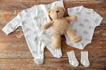 婴儿衣服，婴儿时代和服装概念—紧身衣和袜子与泰迪熊玩具在木桌上。婴儿紧身衣和泰迪熊在木桌上