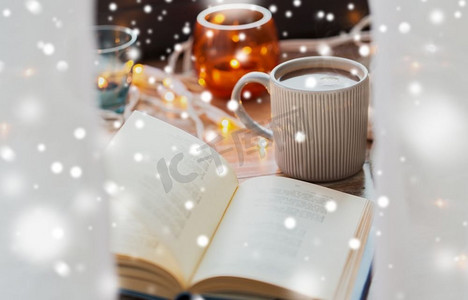 圣诞节、节日和冬天的概念书和一杯咖啡或热巧克力放在雪地上的桌子上。在雪地上看书，喝杯咖啡或热巧克力