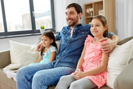 家庭，童年和父亲的概念-快乐的父亲和女儿在家里的沙发上。快乐的父亲和女儿们在家里的沙发上