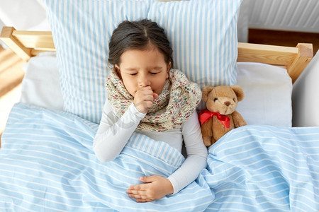 咳嗽摄影照片_健康，儿童和人的概念-生病咳嗽的女孩躺在家里的床上。生病的咳嗽女孩躺在家里的床上
