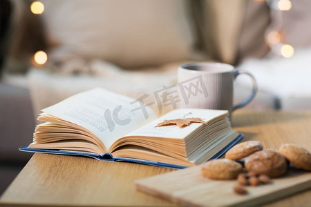 舒适舒适的家概念书，秋叶，一杯茶和燕麦饼干放在木桌上。桌上有秋叶、饼干和茶的书