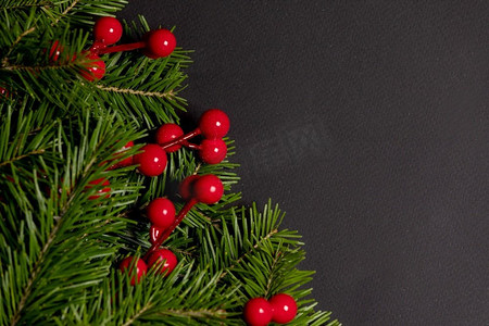 红色卡片装饰摄影照片_松树的树枝和红色的浆果在黑色纸张的背景下平放在顶视模型上。黑纸上的松枝装饰