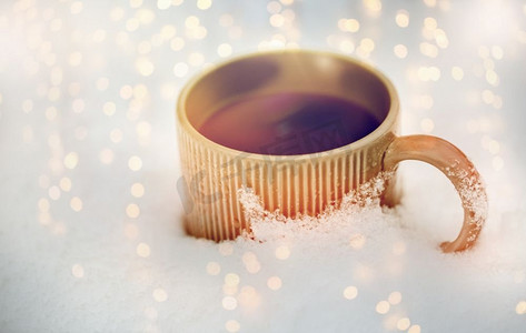 暖咖啡摄影照片_饮料、圣诞节和寒假概念--雪地里的茶杯或咖啡杯。雪地里的茶杯或咖啡杯