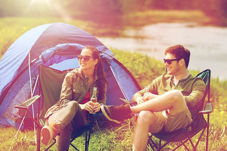 露营、旅行、旅游、徒步旅行和人类概念-在露营帐篷里喝啤酒或苹果酒的幸福夫妇。幸福的情侣在露营帐篷里喝啤酒