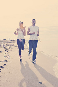 清晨跑步摄影照片_快乐的年轻夫妇清晨在海滩上跑步和慢跑