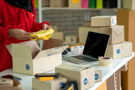 在线卖家在家庭办公室工作,并将运输箱打包给客户.平板手机手机