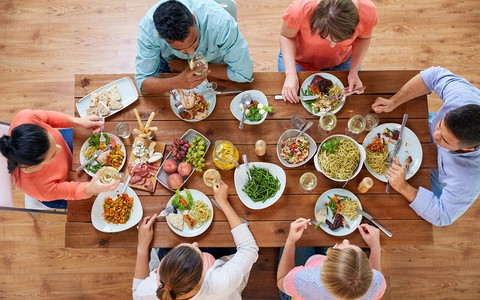 吃喝玩乐摄影照片_吃喝玩乐的概念--一群人在餐桌上与食物一起用餐。一群人带着食物在餐桌上吃饭