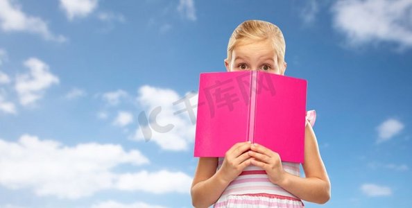 孩子的困惑摄影照片_童年和人的概念—隐藏在书后面的小女孩在蓝天和云背景小女孩隐藏在书在天空背景