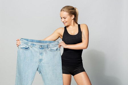 大号摄影照片_饮食、减肥和人们的概念--穿着超大号裤子的年轻苗条的运动女性。穿着超大号裤子的年轻苗条的运动女性