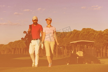 年轻夫妇走到下一个洞在高尔夫球场上。一个拿着高尔夫球袋的男人。夫妇走在高尔夫球场