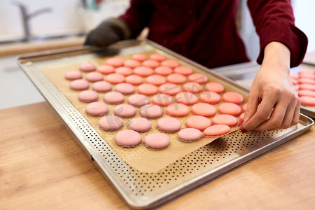 烹饪、糖果和人们的概念-面包店的主厨在烤箱托盘上放马卡龙。糖果店的厨师在烤箱托盘上放马卡龙