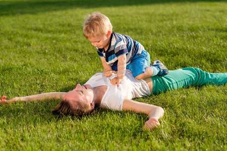 快乐的女人和孩子在草地上玩得很开心。公园里母子俩在绿茵茵的草地上休息的家庭生活场景。