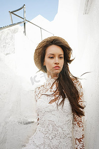 一位身着白色连衣裙、头戴草帽的美女正在圣托里尼岛享受假期。欧洲夏季旅游目的地。希腊群岛