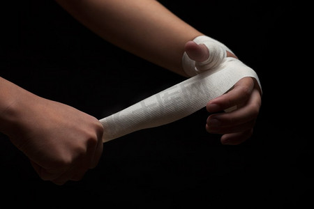 美丽健康的女拳击手正在为战斗或训练做准备，在黑暗的背景下用绷带包裹着手。