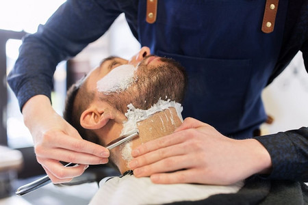 剃胡子的男人摄影照片_美容和人的概念-理发店里留着直剃刀胡子的男人和理发师。留着直剃须刀的男人和理发师