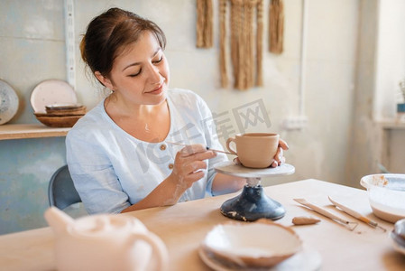女陶工用锅铲剥皮锅，陶艺工作室。女人塑造一个碗。手工陶艺，用粘土制作的餐具