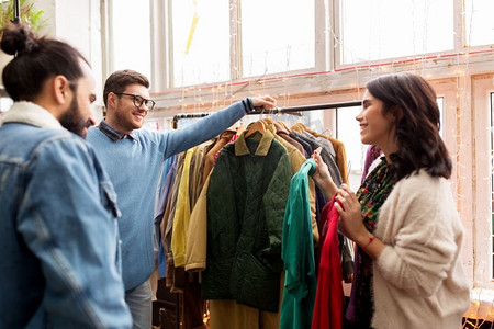 销售、购物、时尚和人概念-朋友选择衣服在复古服装店。朋友们在复古服装店挑选衣服