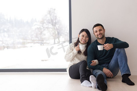 在寒冷的冬日，幸福的年轻多民族夫妇在家中靠窗喝着早晨的咖啡