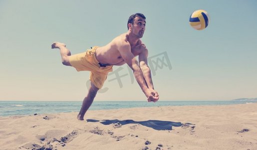 水排球摄影照片_男子沙滩排球运动员在滚烫的沙滩上跳跃