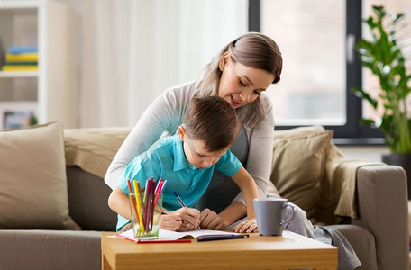 家庭和教育理念-快乐的母亲和小儿子在家里写或画练习册。母子俩在家中拿着练习册