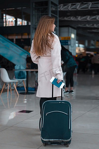 拖着行李旅行摄影照片_年轻的女旅行者在机场大厅拖着行李。机场咖啡馆背景。在机场大厅散步的旅客。