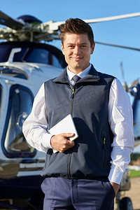 手持数字平板电脑微笑的飞行员站在直升机前的肖像