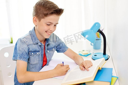 教育、童年和人概念-愉快的学生男孩有书写作对笔记本在家里。学生男孩与书写作笔记本在家里
