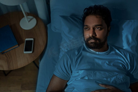 睡眠，失眠和人的概念—spelpess印度男子躺在床上在家里晚上。spelpess印度人躺在床上晚上