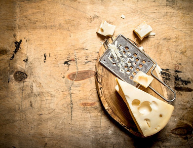 一块奶酪和磨碎机放在地板上。在一张木桌上。一块奶酪和磨碎机放在地板上。