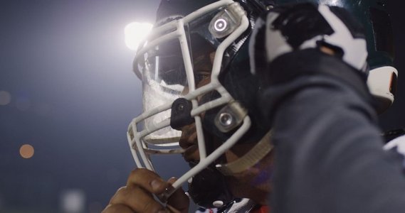 美国橄榄球运动员戴上防护头盔以抵御体育场明亮的照明灯光