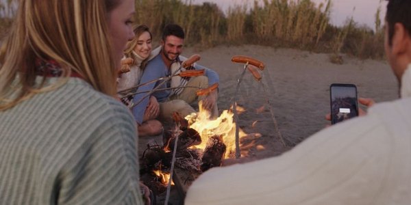 一群年轻的朋友深夜坐在火堆旁，烤着香肠，喝着啤酒，聊天，玩得很开心