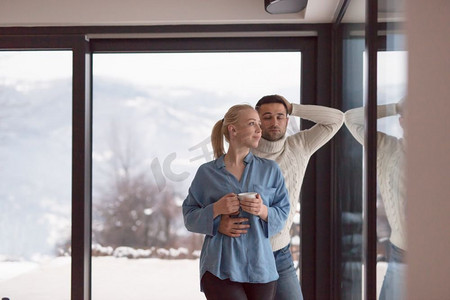 享受在寒冷的冬天晚上的窗的茶的浪漫的年轻夫妇在家