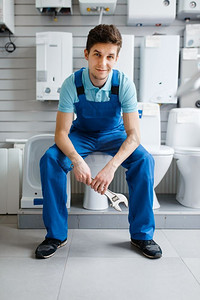 穿着制服的水管工坐在厕所在水管商店的陈列柜。男子在商店购买卫生工程工具和设备