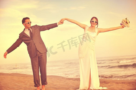 幸福刚刚结婚的年轻夫妇在美丽的日落海滩庆祝和玩乐
