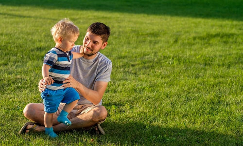 快乐的男人和孩子在草地上享受户外乐趣。公园里父子俩在绿茵茵的草地上休息的家庭生活场景。