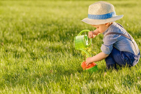 蹒跚学步的孩子的肖像户外。农村场景与一岁的男婴戴草帽使用喷壶