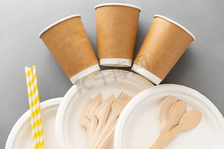 木质盘子和勺子摄影照片_回收利用、餐具和环保概念-灰色背景下的一次性纸质和木质餐具。纸和木制一次性餐具