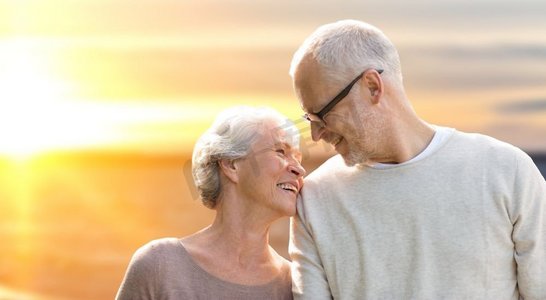 老年、旅游、旅行和人概念-在日落背景的愉快的资深夫妇。愉快的资深夫妇在日落背景