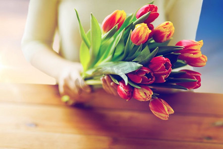 春天郁金香花摄影照片_人物、节日和妇女节的概念--木桌上拿着郁金香花的女人的特写。女子手持郁金香花朵的特写