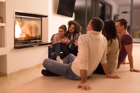 一群年轻的多民族夫妇坐在地板上在壁炉前在寒冷的冬夜