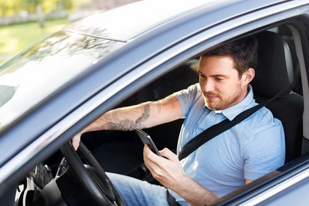 交通、车辆和科技概念-微笑的人或司机驾驶汽车和使用智能手机。开车和使用智能手机的男人