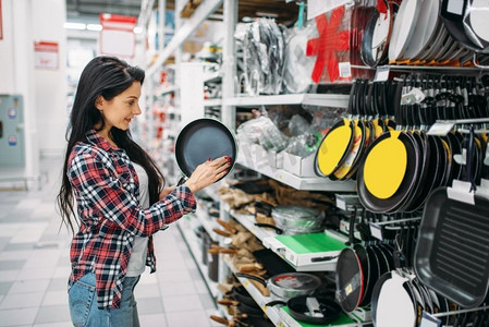 家电卖场开业摄影照片_一名年轻女子在超市选购煎锅。女性顾客在大卖场购物，厨房产品