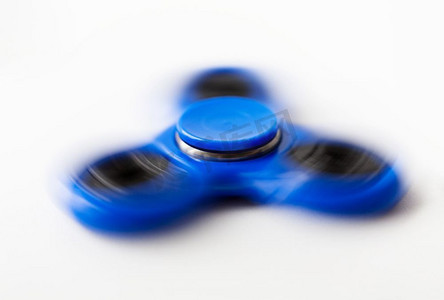玩具，娱乐和行动-蓝色旋转的坐立不安的微调器特写镜头在白色背景。近摄蓝色纺纱坐立不安微调