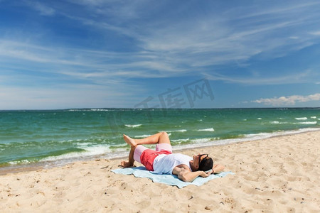 年轻人海边摄影照片_暑假和人们的概念-快乐微笑的年轻人在沙滩毛巾上日光浴。快乐微笑的年轻人在沙滩毛巾上晒日光浴