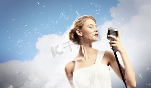 金发女歌手。金发女歌手闭着眼睛拿着麦克风在云彩的背景下
