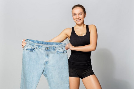 饮食、减肥和人们的概念--穿着超大号裤子的年轻苗条的运动女性。穿着超大号裤子的年轻苗条的运动女性