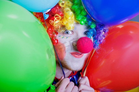 微笑的小丑手持一堆五颜六色的气球。幽默的马戏团概念。拿着一堆彩色气球的小丑。
