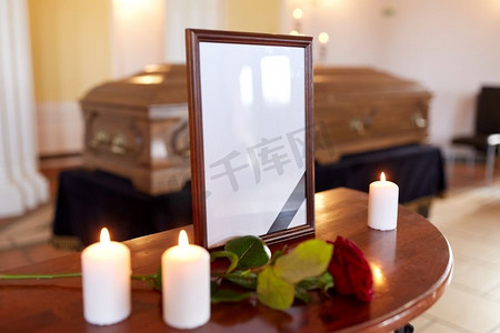 哀悼摄影照片_葬礼和哀悼的概念-相框与黑丝带，燃烧的蜡烛和棺材在教堂。教堂葬礼上的相框和棺材